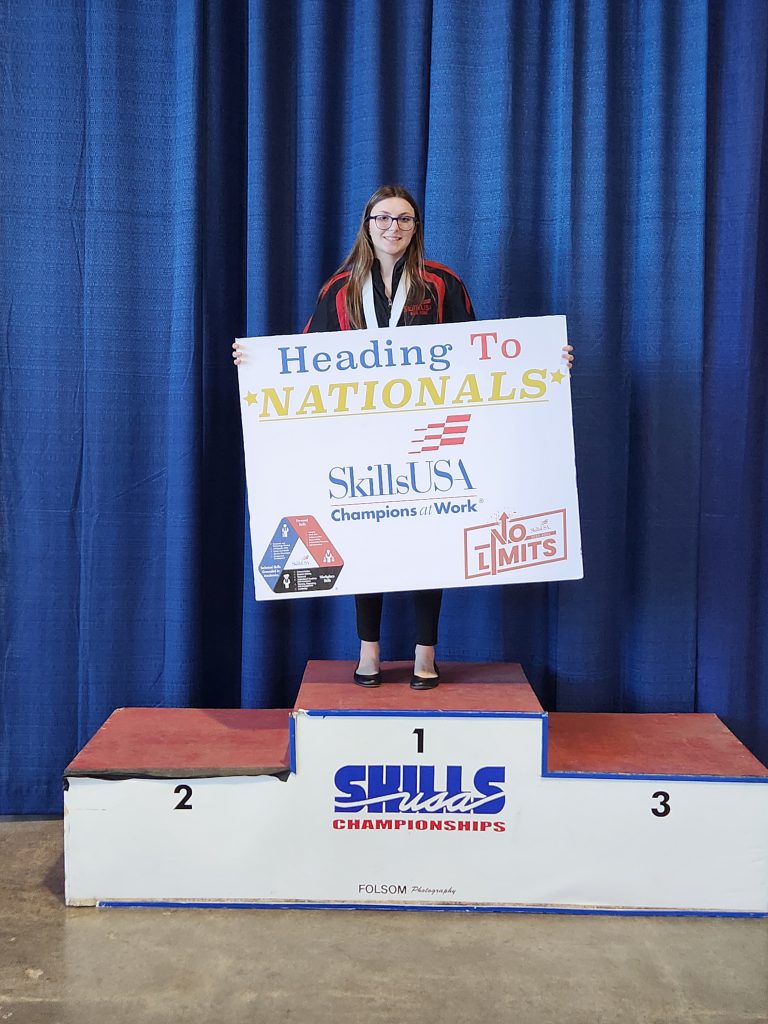 Zoey Caldwell on the podium at the state SkillsUSA conference holding a sign stating that she's going to nationals