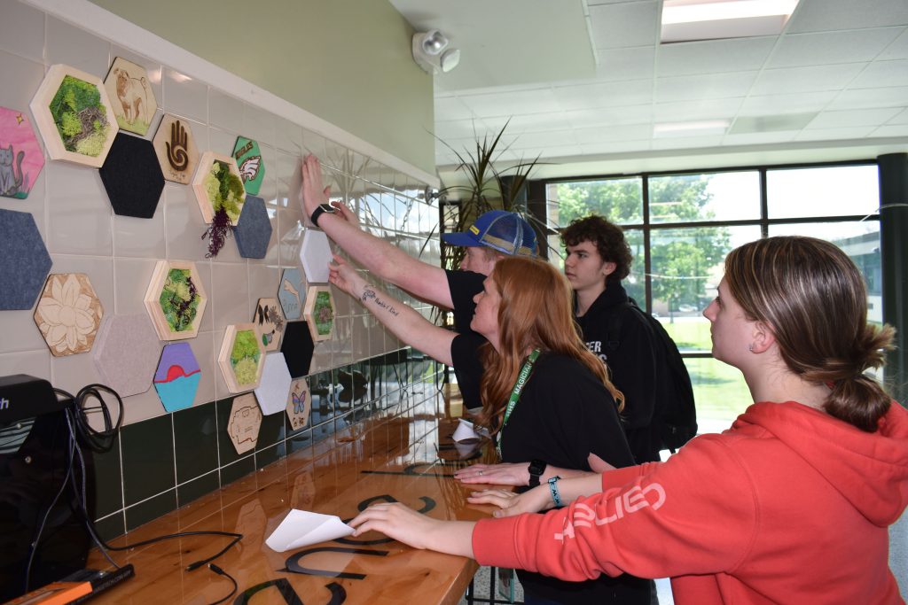 Art teacher and art and ag students putting up new moss art wall