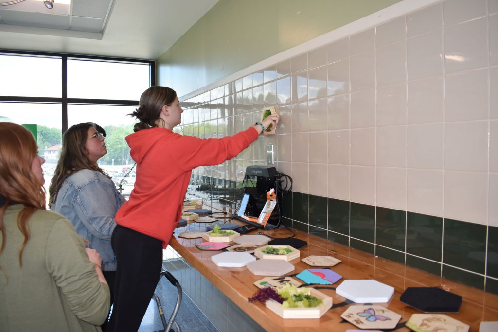 Student putting up first piece of new moss art wall with teachers watching