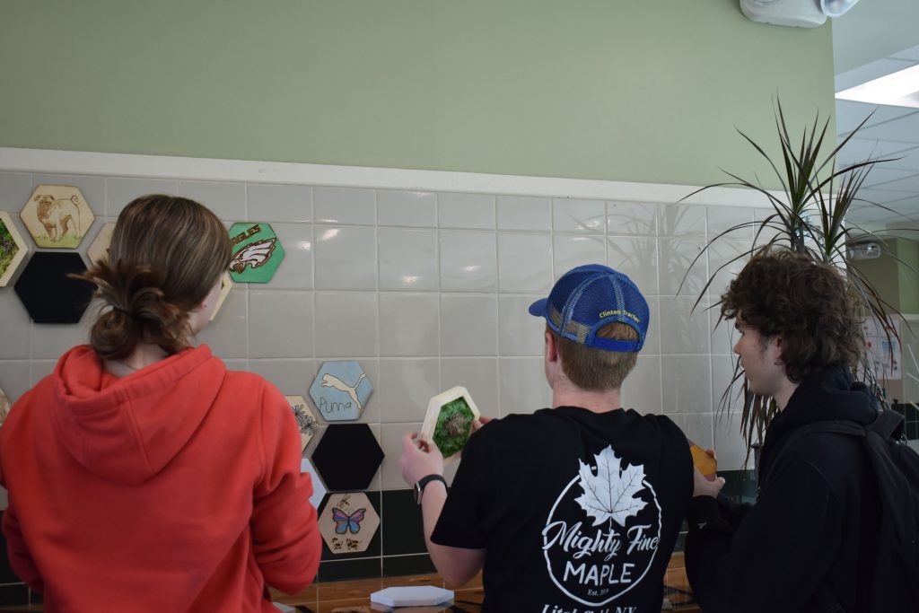 Three students putting up moss art wall display