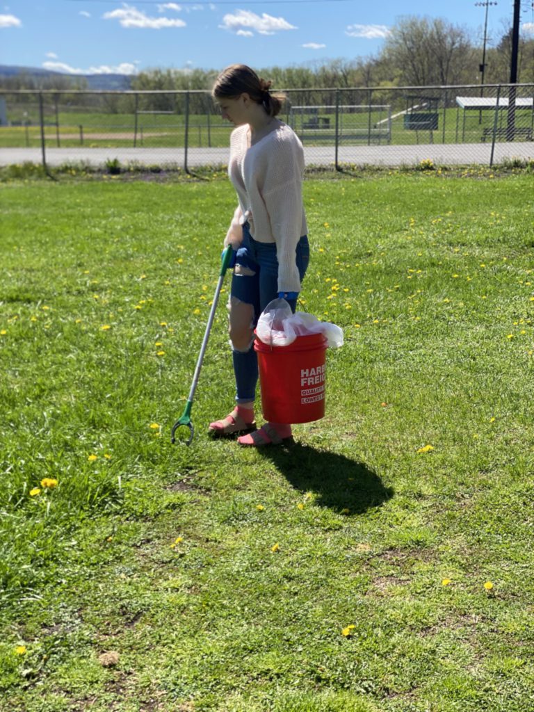 Student cleaning up at Harmon Park in grass field