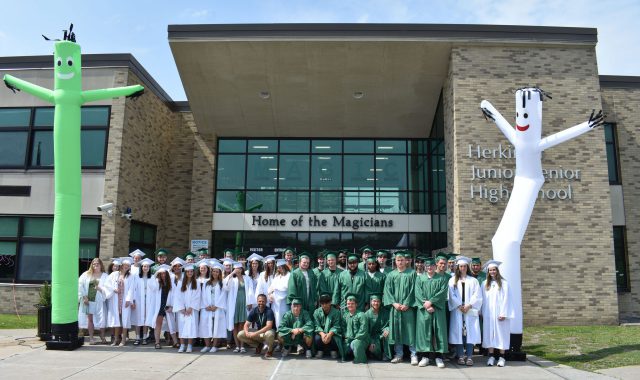 Seniors posing in front of the high school in caps and gowns with large balloon creatures