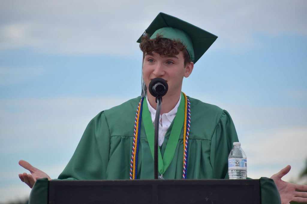 A student wearing cap and gown speaks at the podium at graduation.