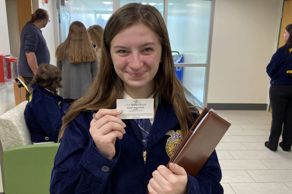 A Future Farmers of America student proudly displays the business card of the president of State University of New York Morrisvile.