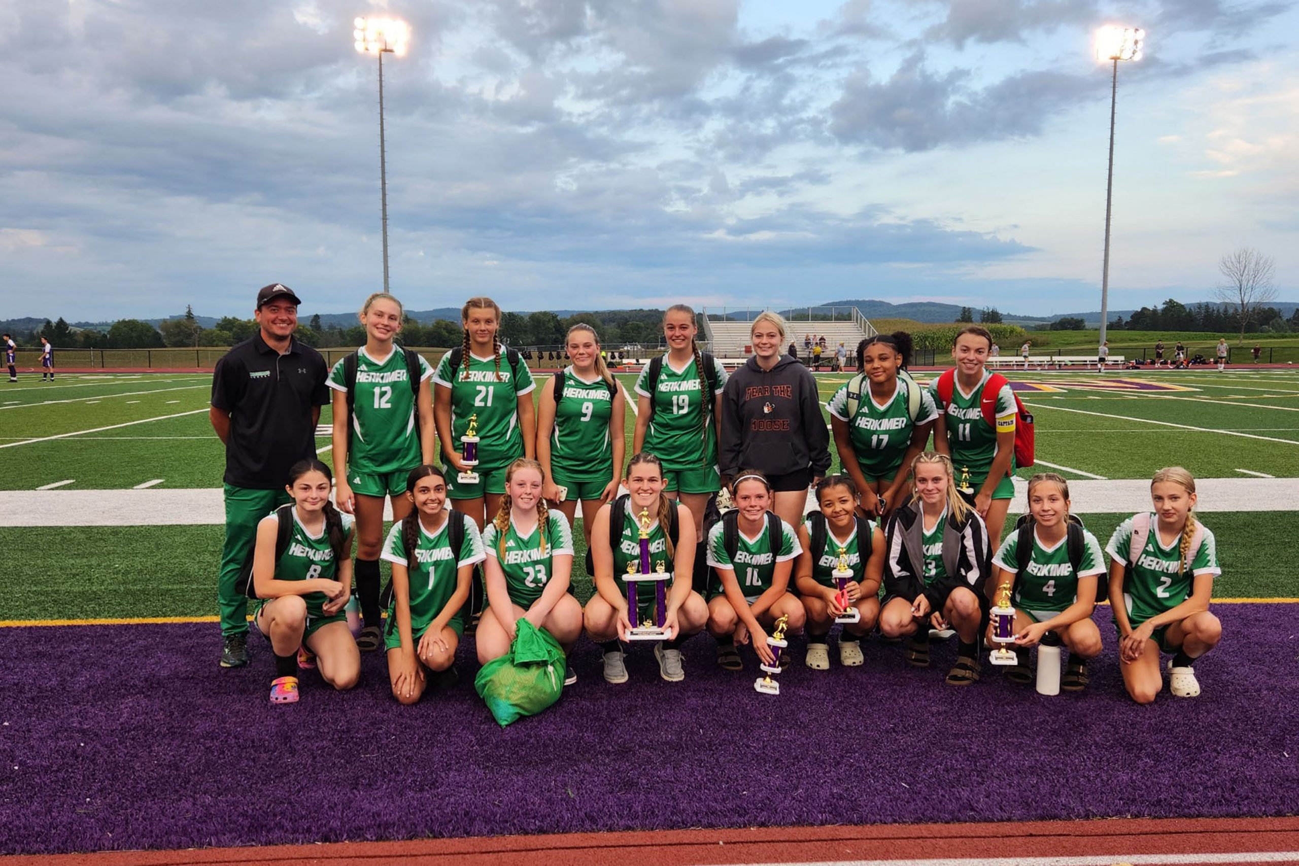 Athletes smile on the field with their trophies