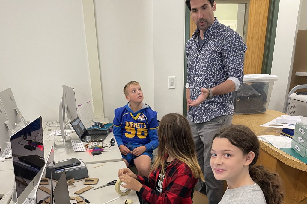 A teacher engages with three students in a computer lab.