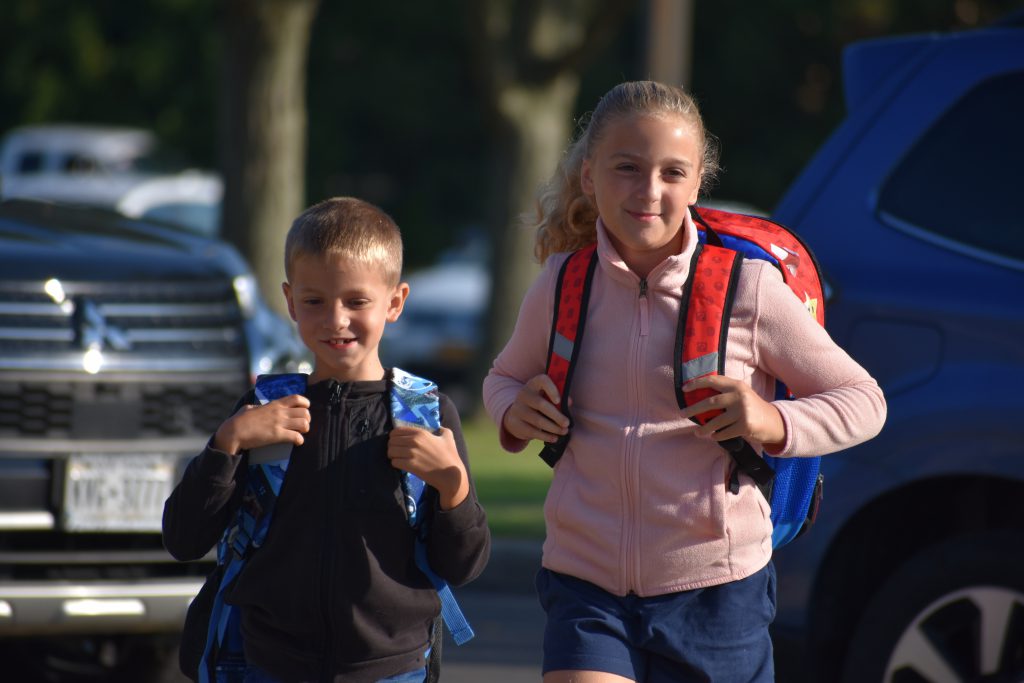 Two students grip their colorful backpacks in the sunlight as they walk toward the school entrance