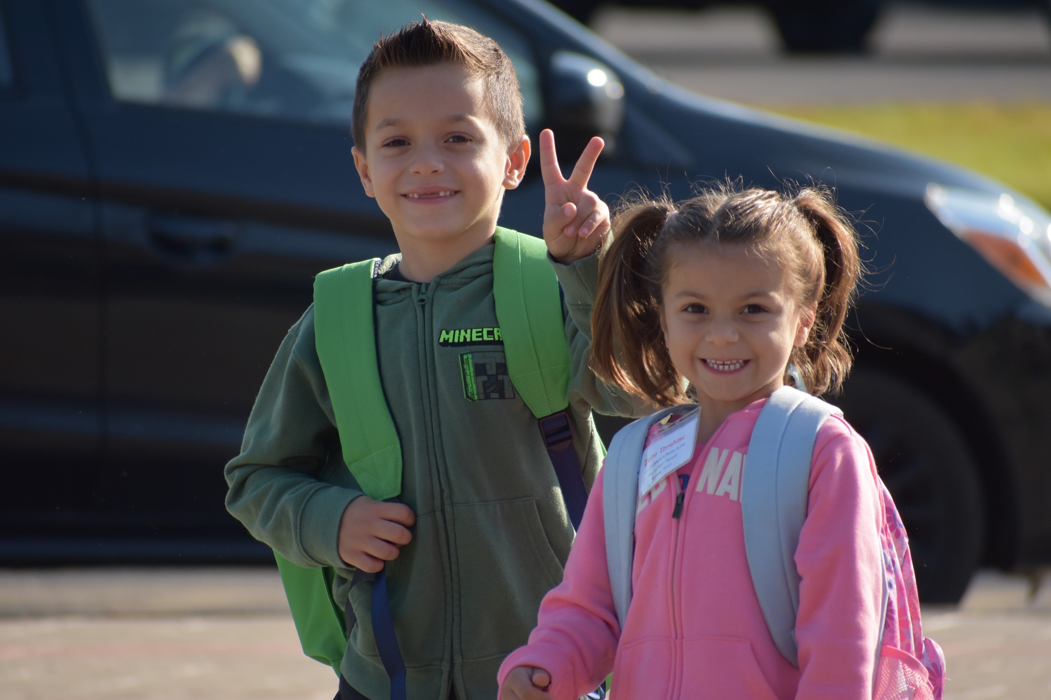 Two elementary aged children smiling broadly upon arriving at school on the first day