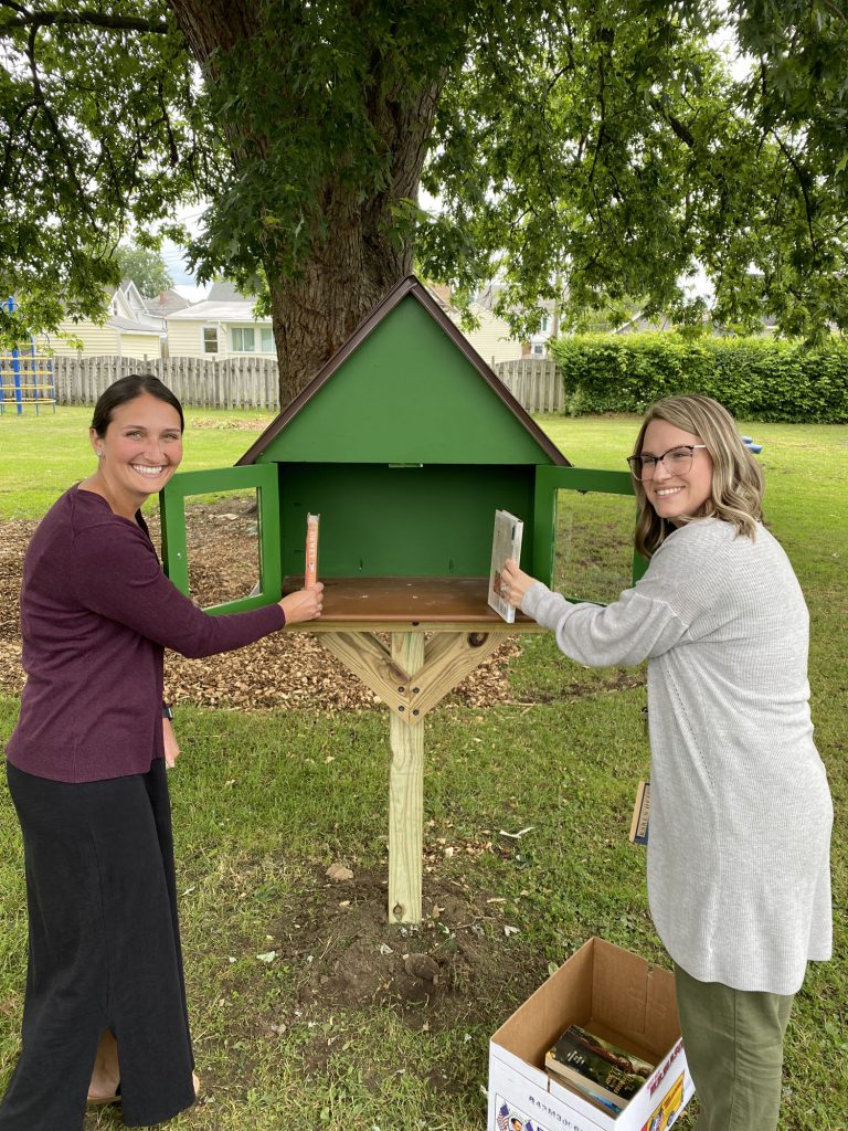 Two staff members putting books in Little Free Library at Harmon Park