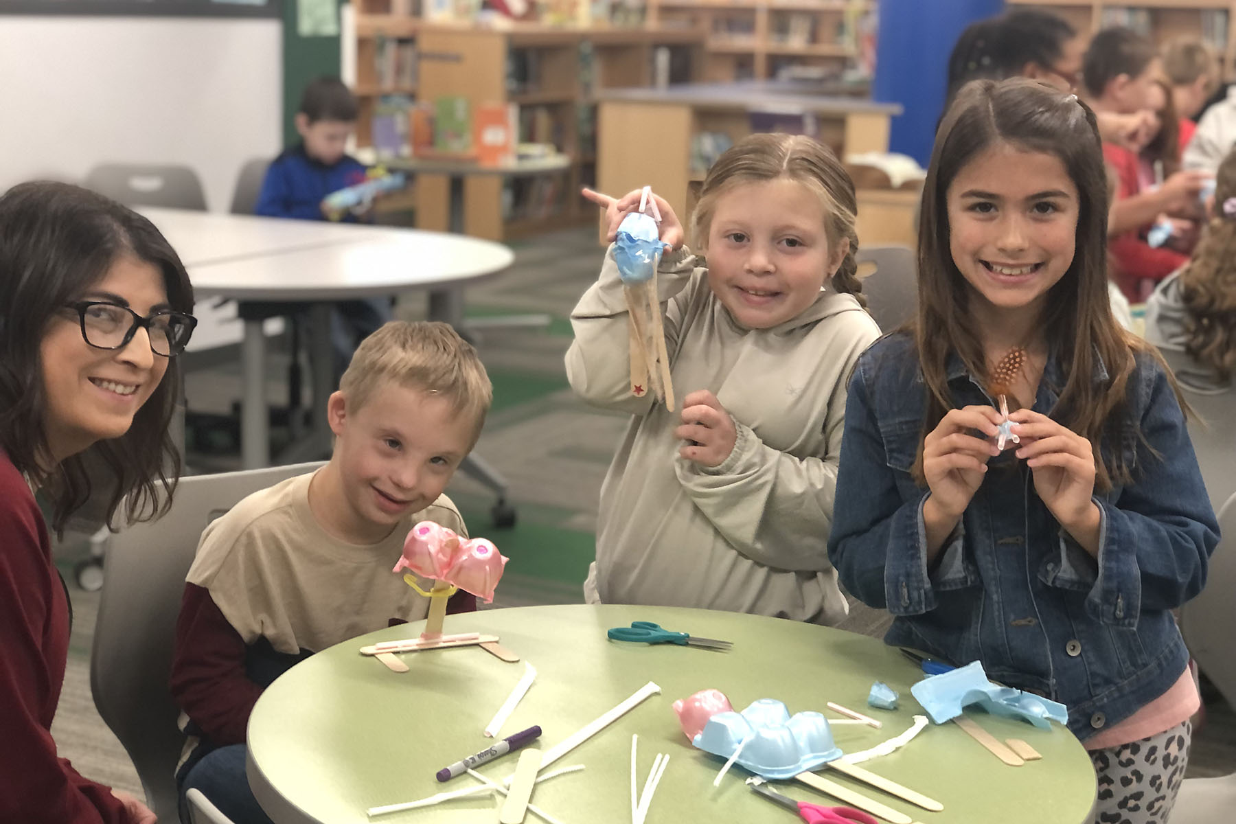 Students in library holding up projects