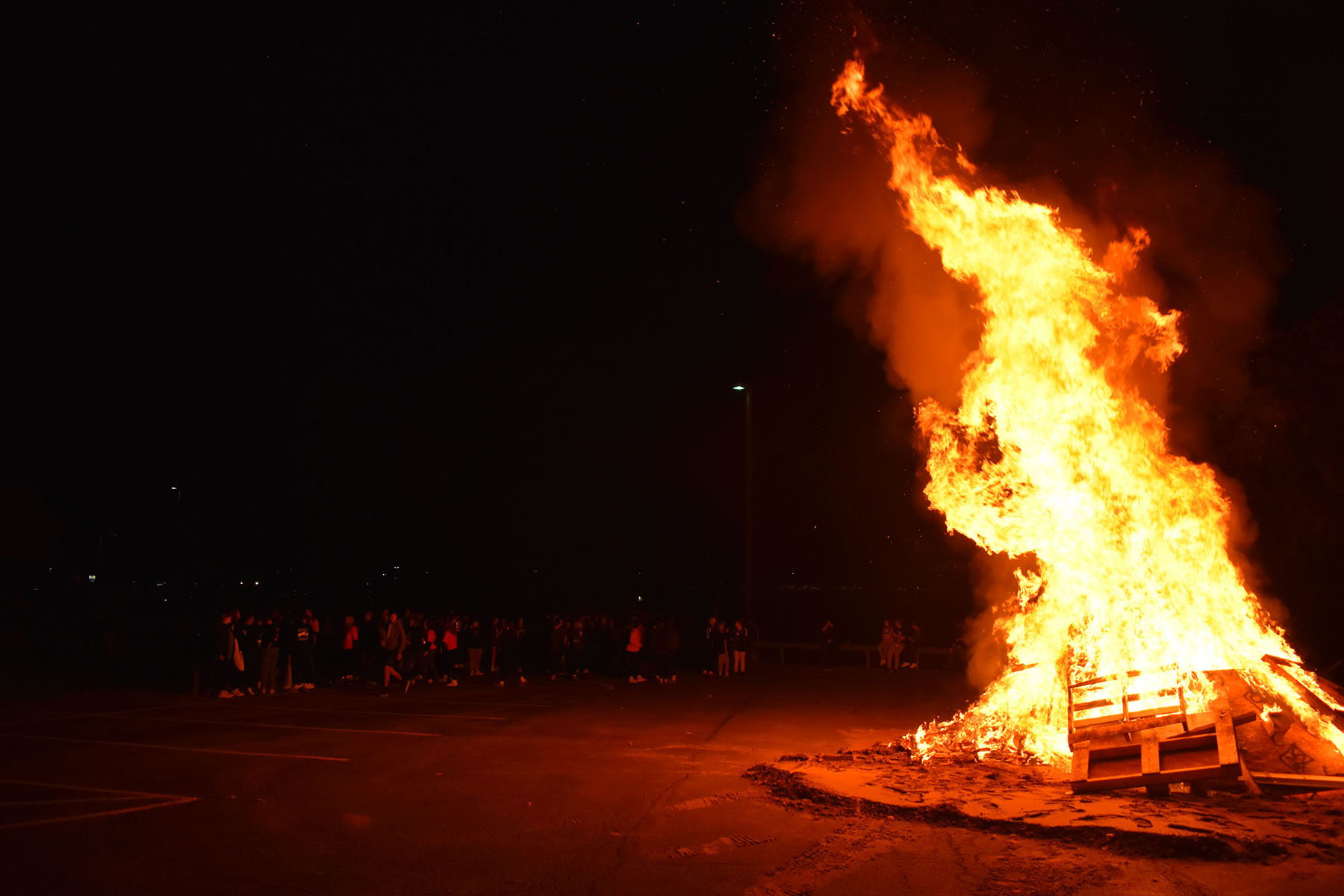 Large bonfire in the dark with students standing nearby in the parking lot