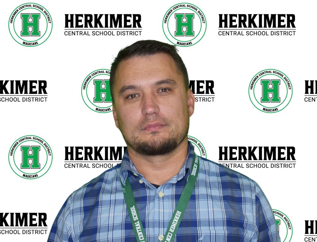 Herkimer Board of Education member Aleksander Verenich in front of Herkimer logos background