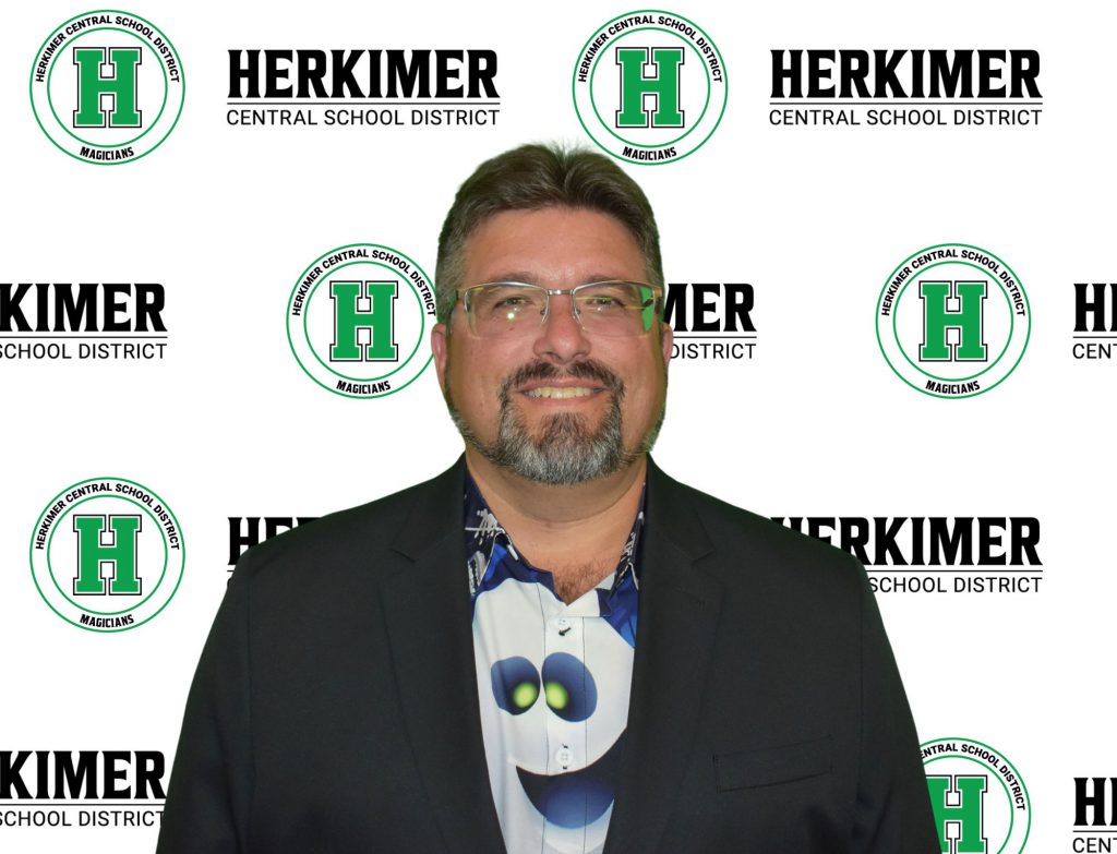 Herkimer Board of Education President Brian Crandall in front of Herkimer logos background