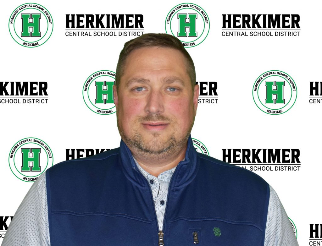 Herkimer Board of Education member Joseph Lamanna in front of Herkimer logos background