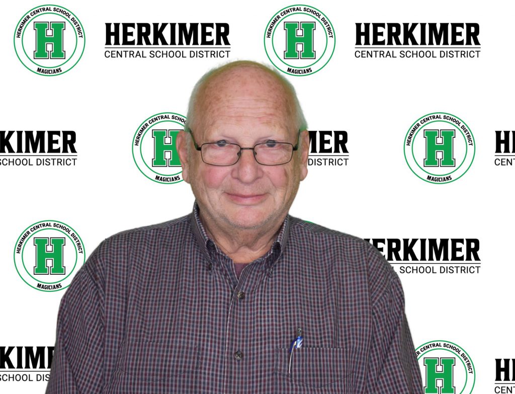 Herkimer Board of Education member Robert Mihevc in front of Herkimer logos background