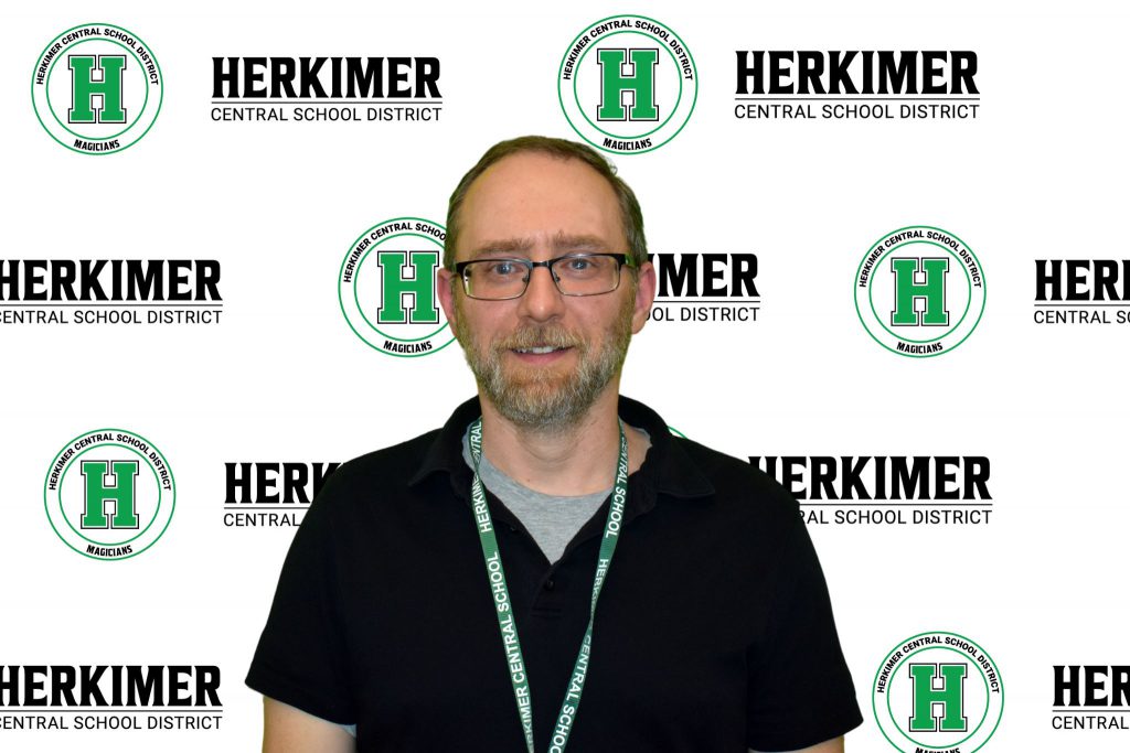 Board of Education member Matthew Collis in front of a Herkimer logos background