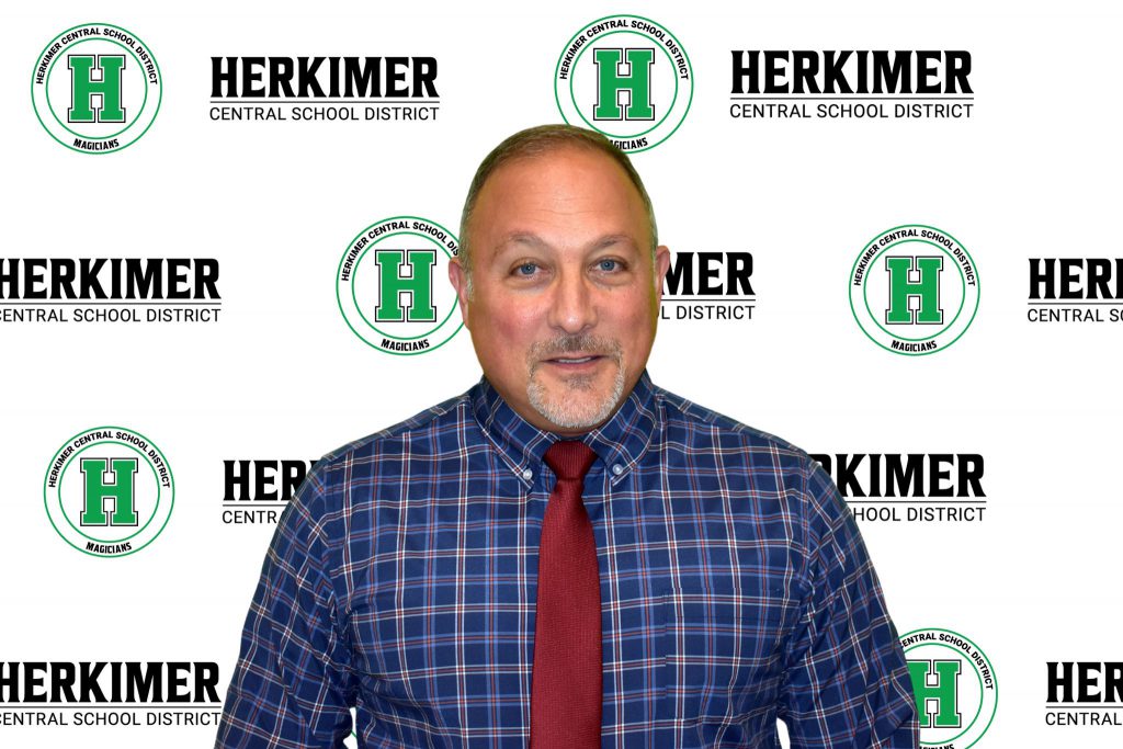 Board of Education member Scott Petucci in front of a Herkimer logos background